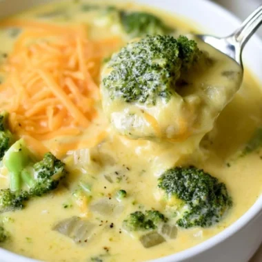 Bowl of cozy keto broccoli cheese soup topped with shredded cheese and fresh herbs.